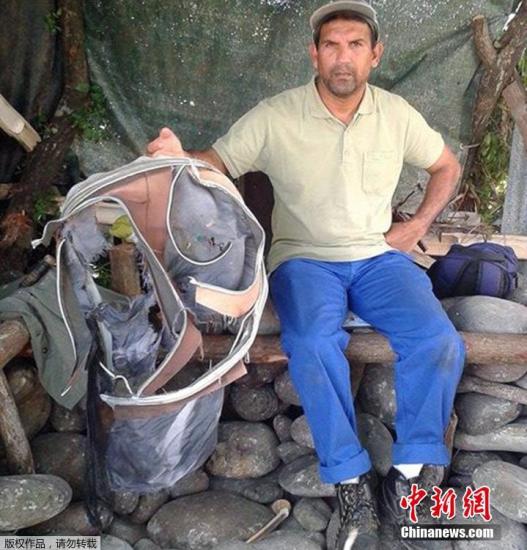 圖為當地時間7月30日，留尼旺島上的一名海岸清潔人員展示他找到的一個手提箱的殘骸。